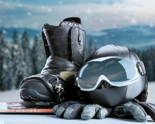 Winter sport glasses, snowboarding boot, helmet and gloves on winter forest and mountains background